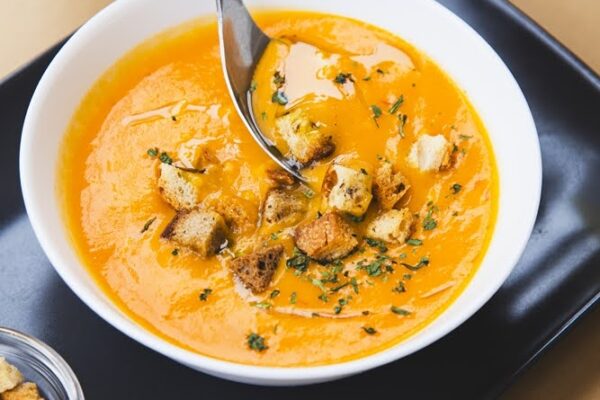 Prato preto, com prato branco com uma sopa de legumes com crutons e ervas